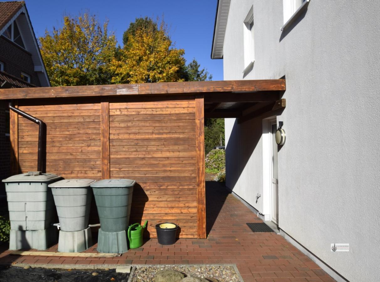 Holzhaus frisch gestrichen mit Regenwassertonnen und Türüberdachung